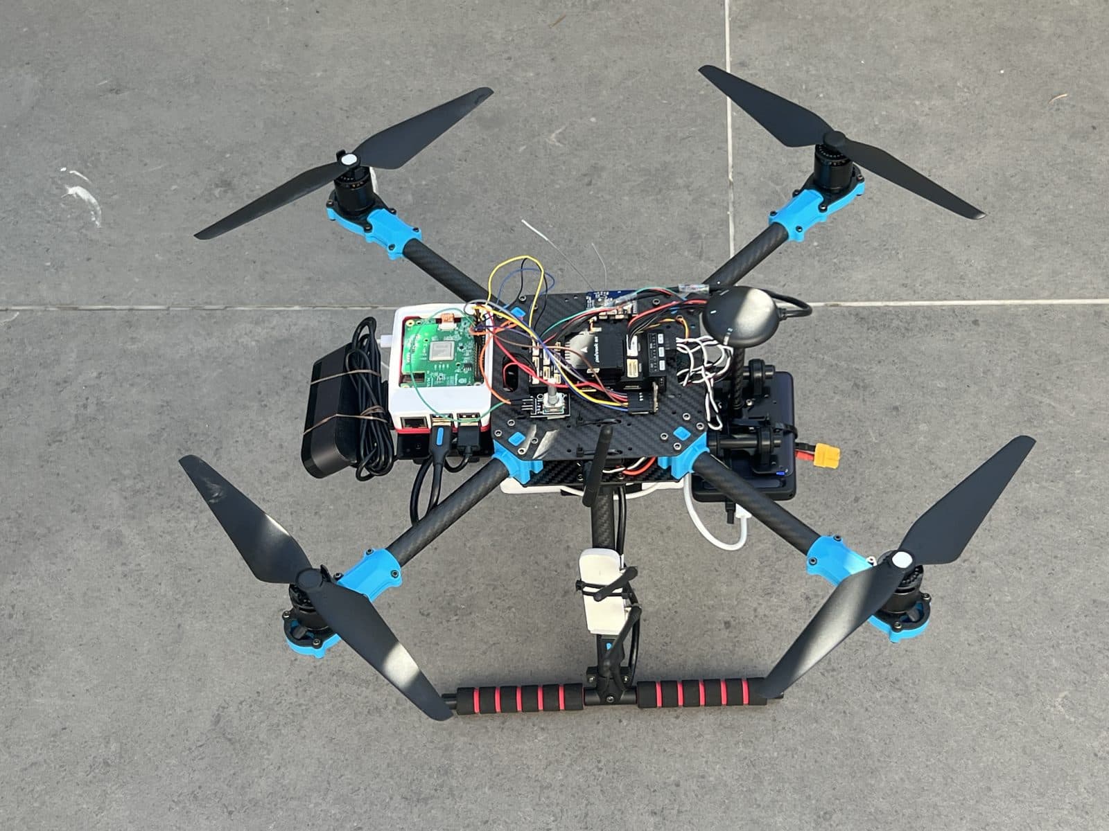 Vista lateral elevada del conjunto de electrónica a bordo: la Raspberry Pi 5 con su HAT Hailo-8 junto a la Pixhawk 6X, el cableado de alimentación y datos, la antena y el pack de batería