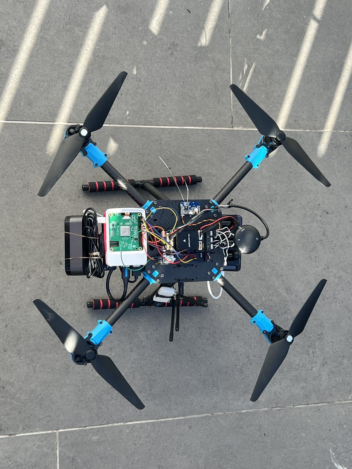 Detalle cenital de la integración de los dos cerebros: la Pixhawk 6X, el hub USB, la Raspberry Pi 5 en su carcasa y el mazo de cables que los une, sobre la placa central de fibra de carbono