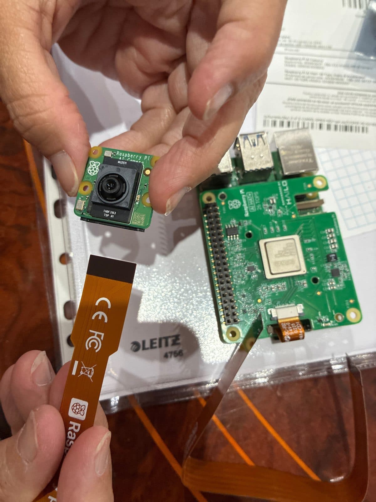 Sujetando la cámara Raspberry Pi y su cable plano, con el HAT Hailo-8 apoyado al fondo
