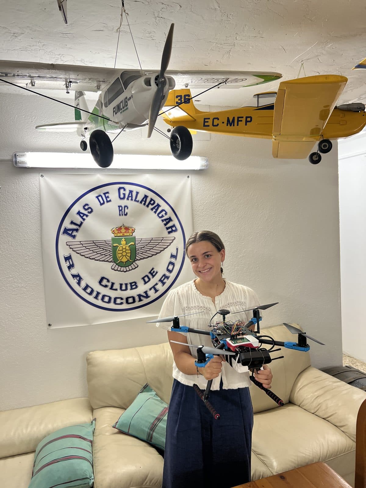 Nerea Gorostidi con el dron Guardian Eye en la sede del Club Alas de Galapagar, bajo el logo del club y varios aviones de aeromodelismo colgados del techo